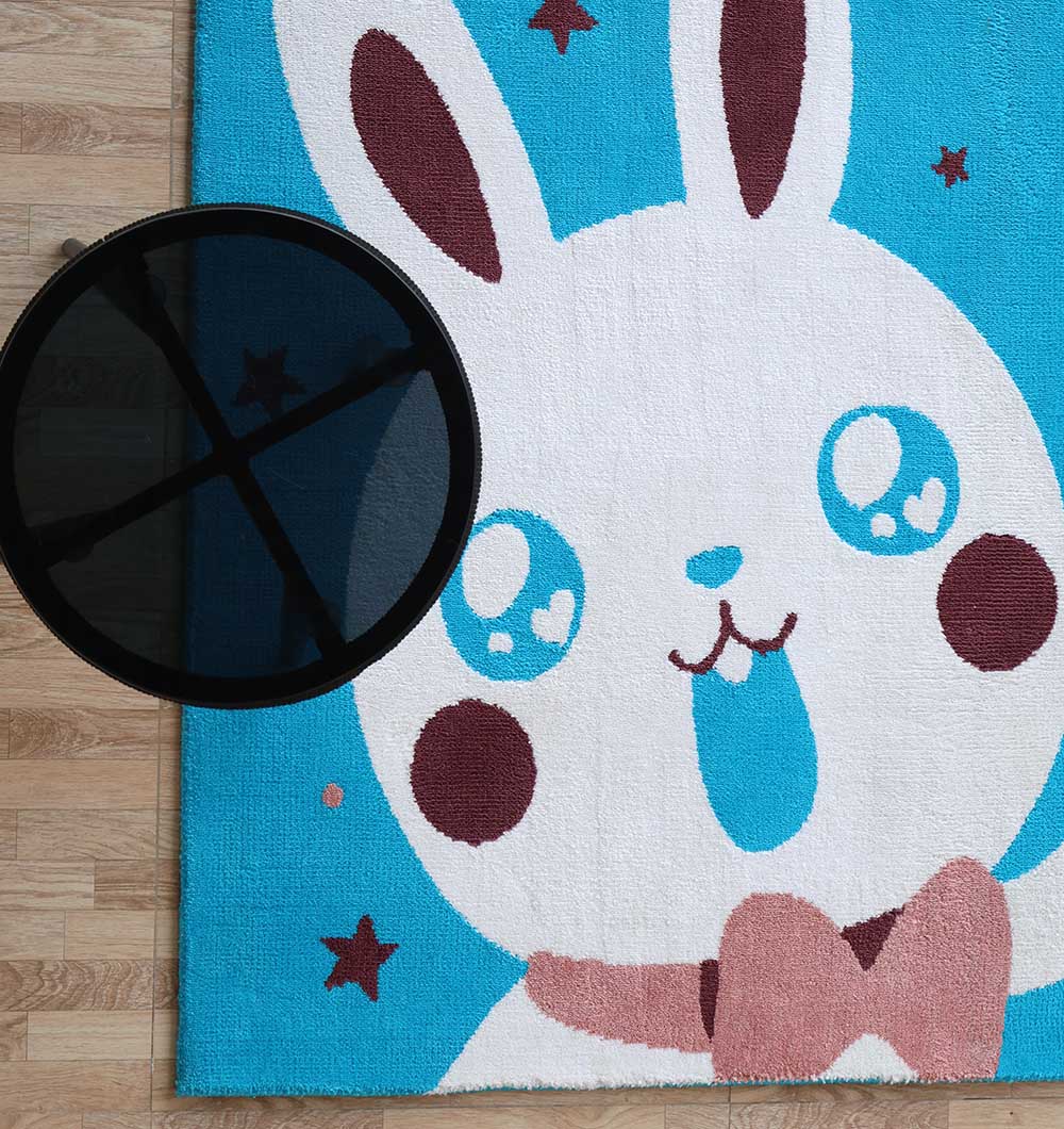 A round black table sits on the RAMSHA HOME Multi Color Kids Area Carpet - KD 011 (120x180 cm), featuring a cartoon bunny face design. This durable polyester rug adds vibrant, kid-friendly decor to light wooden floors.