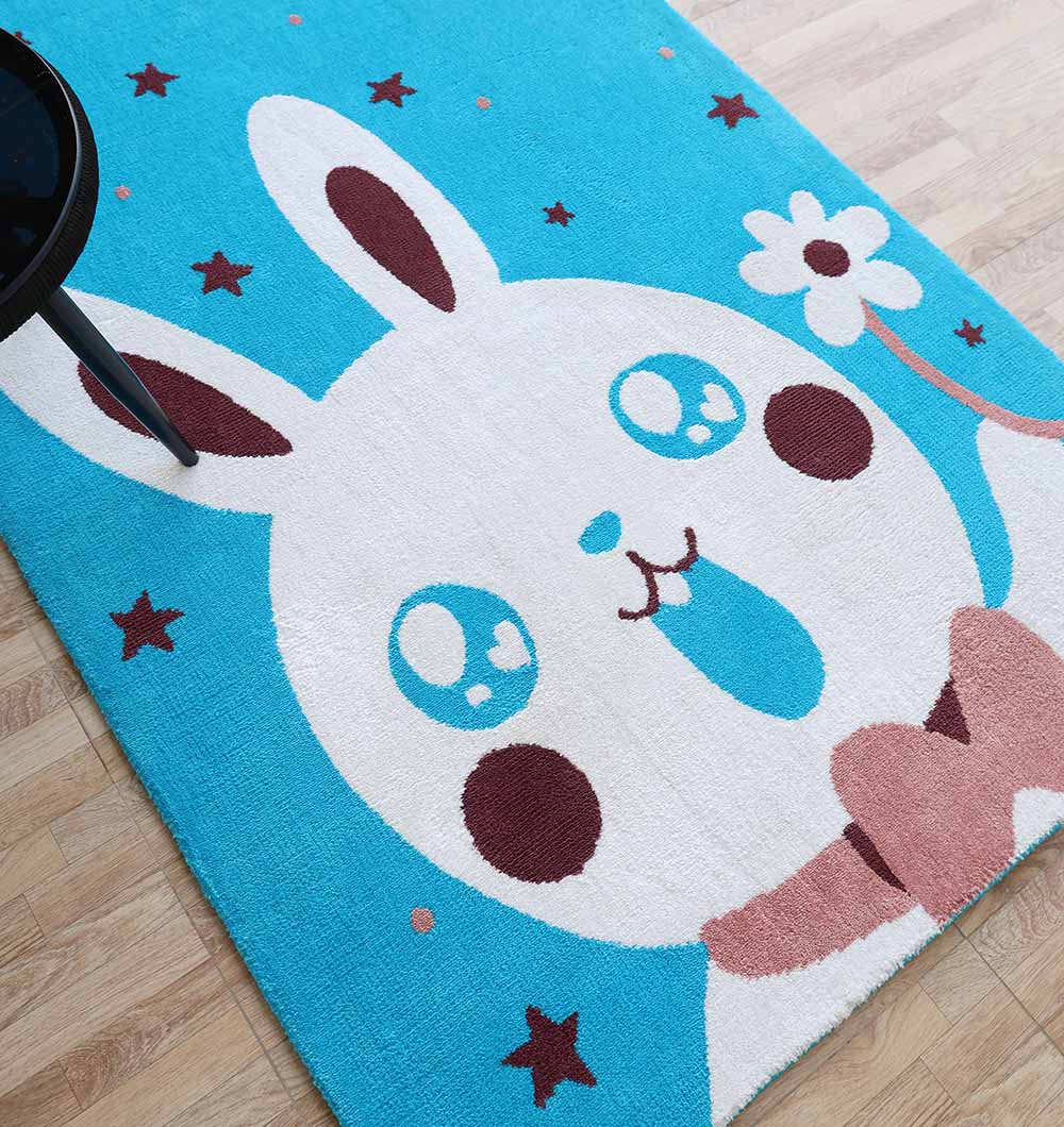 The RAMSHA HOME Multi Color Kids Area Carpet - KD 011 (120x180 cm) is a durable polyester bunny rug with large-eyed cartoon bunny, pink bow tie, and stars—ideal for kid-friendly decor on a light wood floor.