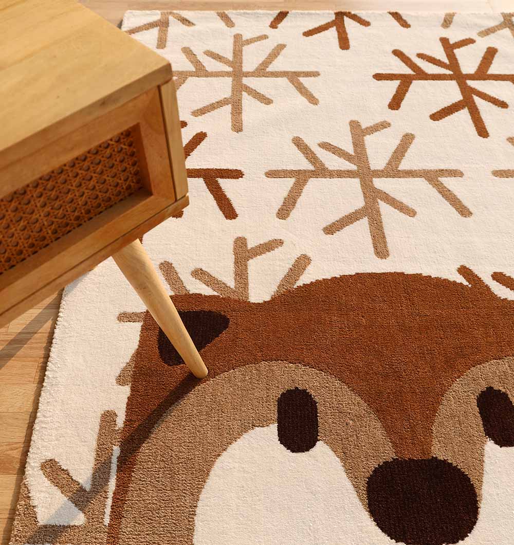A close-up of the RAMSHA HOME Kids Bear Face Beige & Brown Rug – KD 014, a polyester area rug featuring a cute bear face and brown snowflake patterns. A wooden table with angled legs appears in the upper left corner.