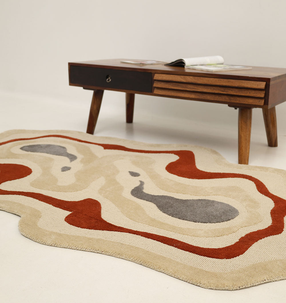 The RAMSHA HOME Amoeba Shaped Multi Color High Low Pile Rug (130x200 cm – KD 016) featuring beige, red, and gray abstract shapes lies on a white floor before a mid-century modern wooden coffee table with an open magazine.