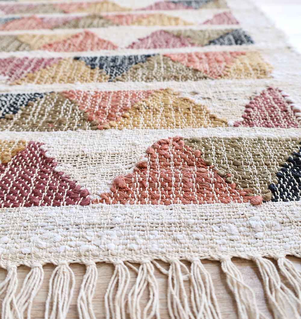 A close-up of the RAMSHA HOME Geometric Jute Tribal Kilim Rug – KLM 003 (170x240cm), featuring colorful earthy-toned triangles, natural jute texture, and a fringed edge.