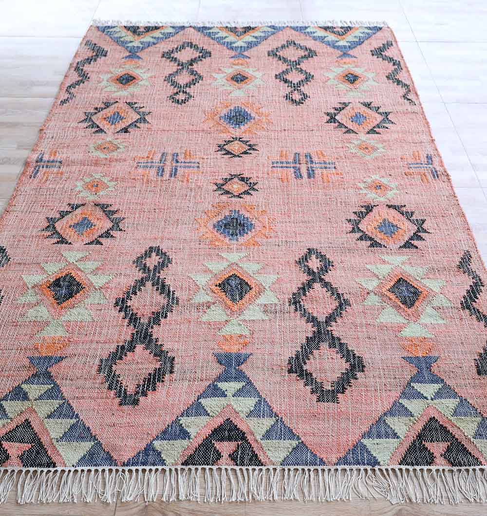 The Handwoven Jute Flatweave Pink Kilim Rug – KLM 005 (170x240cm) by RAMSHA HOME features a tribal diamond and zigzag design in pink, blue, orange, and cream with fringed ends—perfect for adding charm to light wood floors.