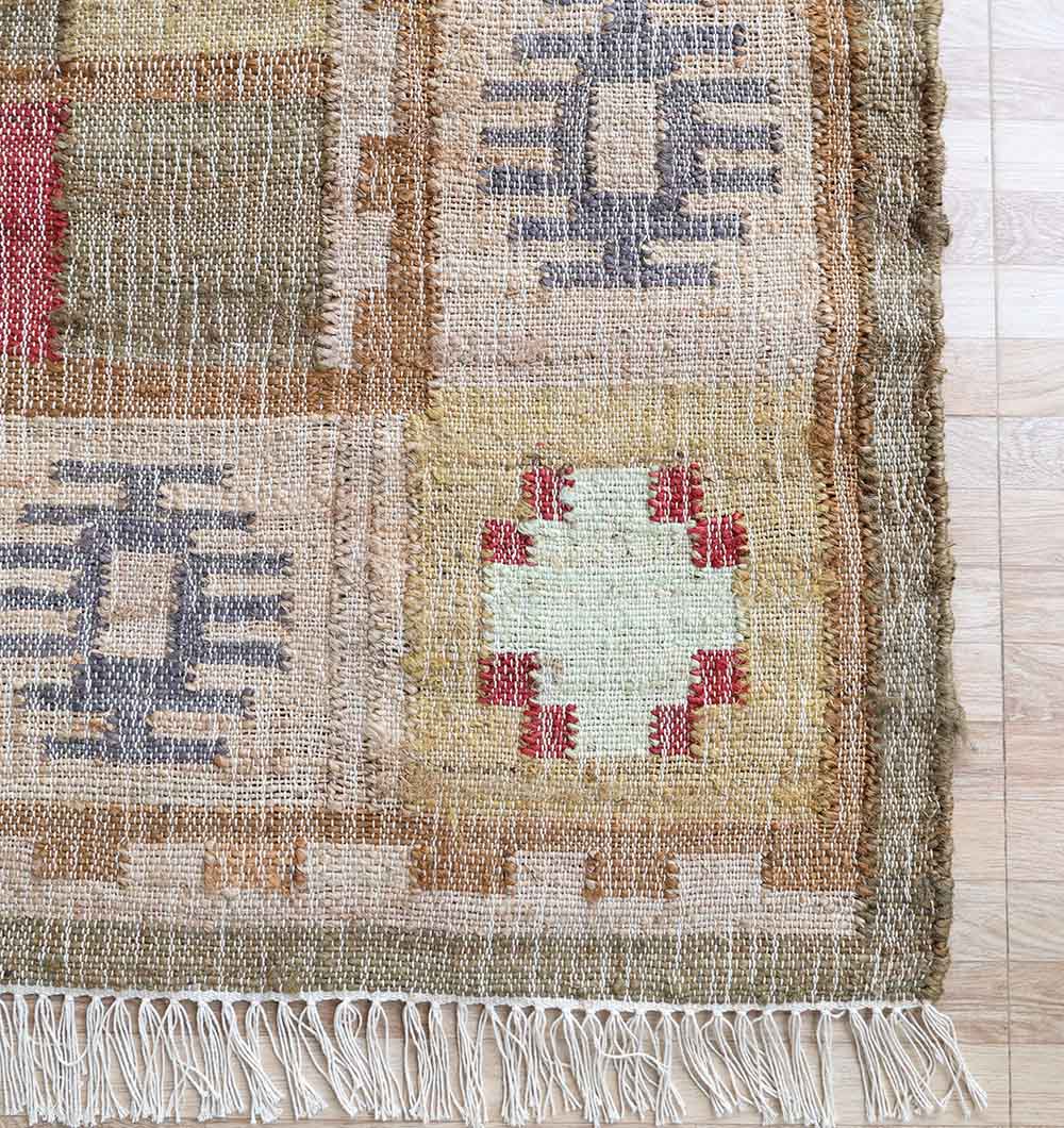 A close-up of RAMSHA HOME’s Symmetrical Bordered Traditional Kilim Rug - KLM 007 (170x240cm), a bohemian flatweave with geometric patterns in beige, brown, gray, and red hues, fringed edges, displayed on a light wood floor.