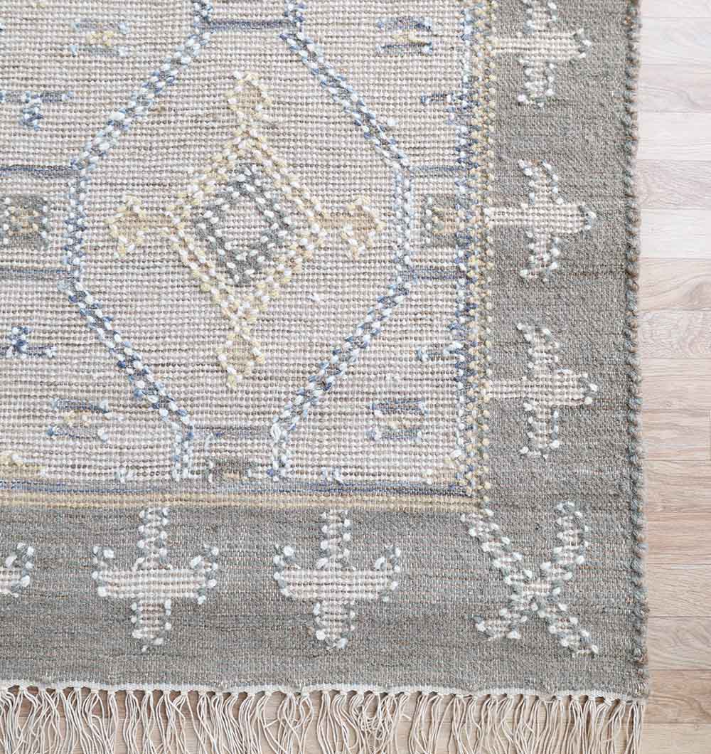 The RAMSHA HOME Neutral Diamond Geometric Flatweave Kilim Rug - KLM 009 (170x240cm) features beige, gray, and light blue diamond patterns with a cross-border design and fringe, complementing light wood floors beautifully.