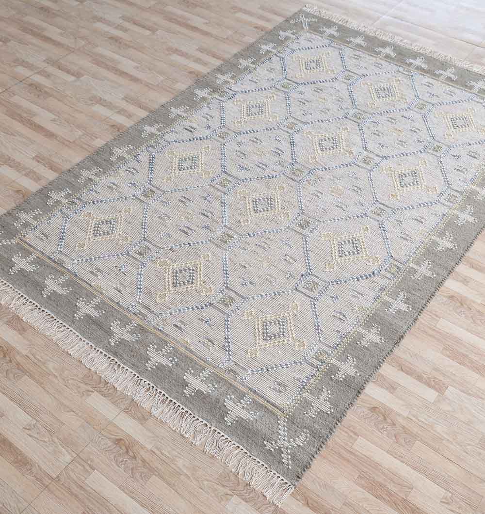 The RAMSHA HOME Neutral Diamond Geometric Flatweave Kilim Rug - KLM 009 (170x240cm) features grey and beige geometric patterns, a gray border with white motifs, and fringed edges, displayed on a light wood floor.