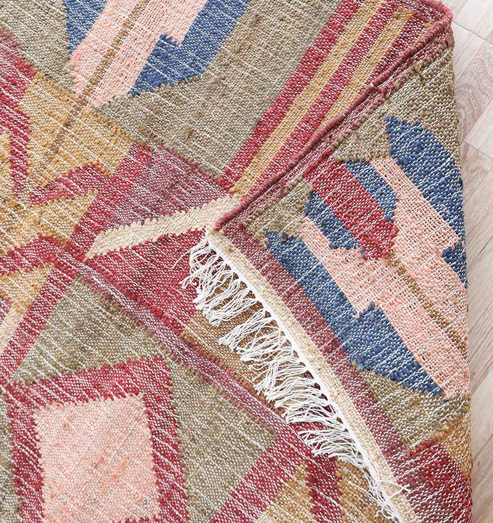 Close-up of the Handwoven Diamond Patterned Kilim Rug - KLM-010 (170x240cm) by RAMSHA HOME, showing its red, pink, blue, and beige geometric patterns and fringed edge on a light wooden floor.