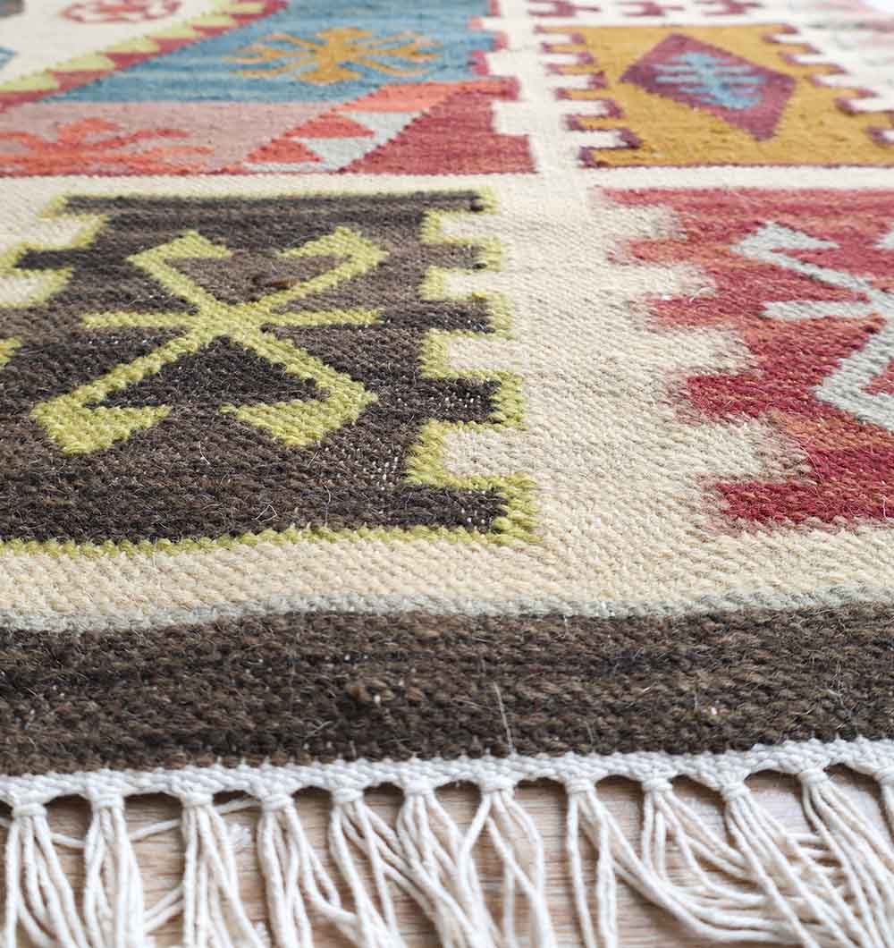 Close-up of the RAMSHA HOME Authentic Turkish Geometric Kilim Rug (KLM 013), showcasing vibrant brown, yellow, red, and blue geometric patterns, a textured surface, and a white fringed edge.