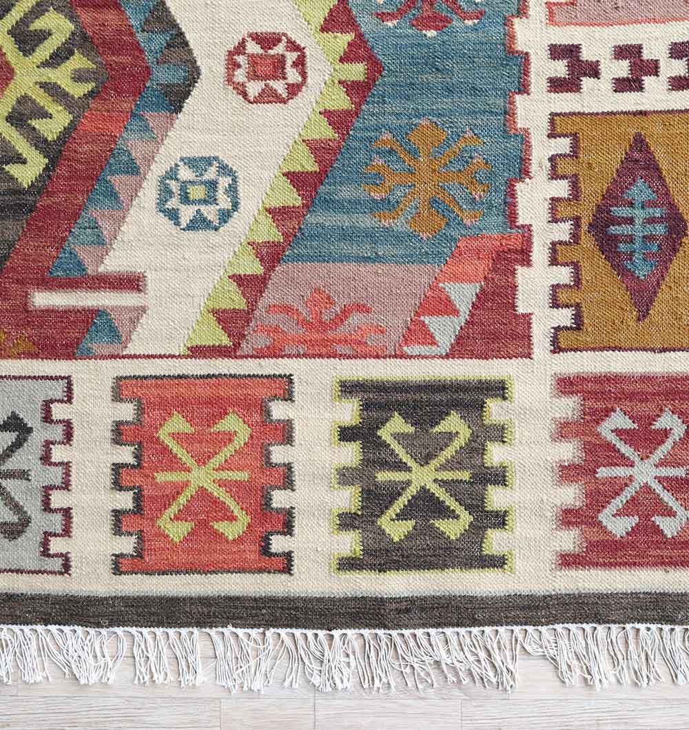 The Authentic Turkish Geometric Kilim Rug - KLM 013 by RAMSHA HOME features vibrant red, blue, yellow, green, and cream geometric patterns with fringe edging and assorted motifs in rectangular and triangular sections.
