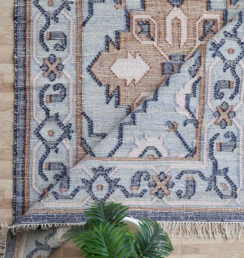 The RAMSHA HOME Kilim Rug Blue Multicolor Tribal Flatweave KLM-015 (170x240 cm) is shown with one corner flipped to display the underside, alongside a green leafy plant at the bottom of the image.