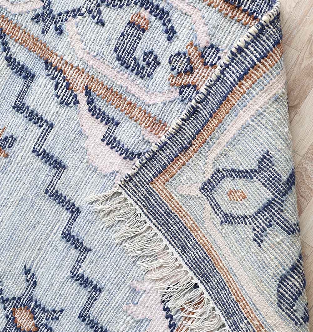 Close-up of the RAMSHA HOME Kilim Rug Blue Multicolor Tribal Flatweave KLM-015 (170x240 cm), partially folded to reveal fringe and weave texture, showcasing its geometric and floral patterns on a wooden floor.