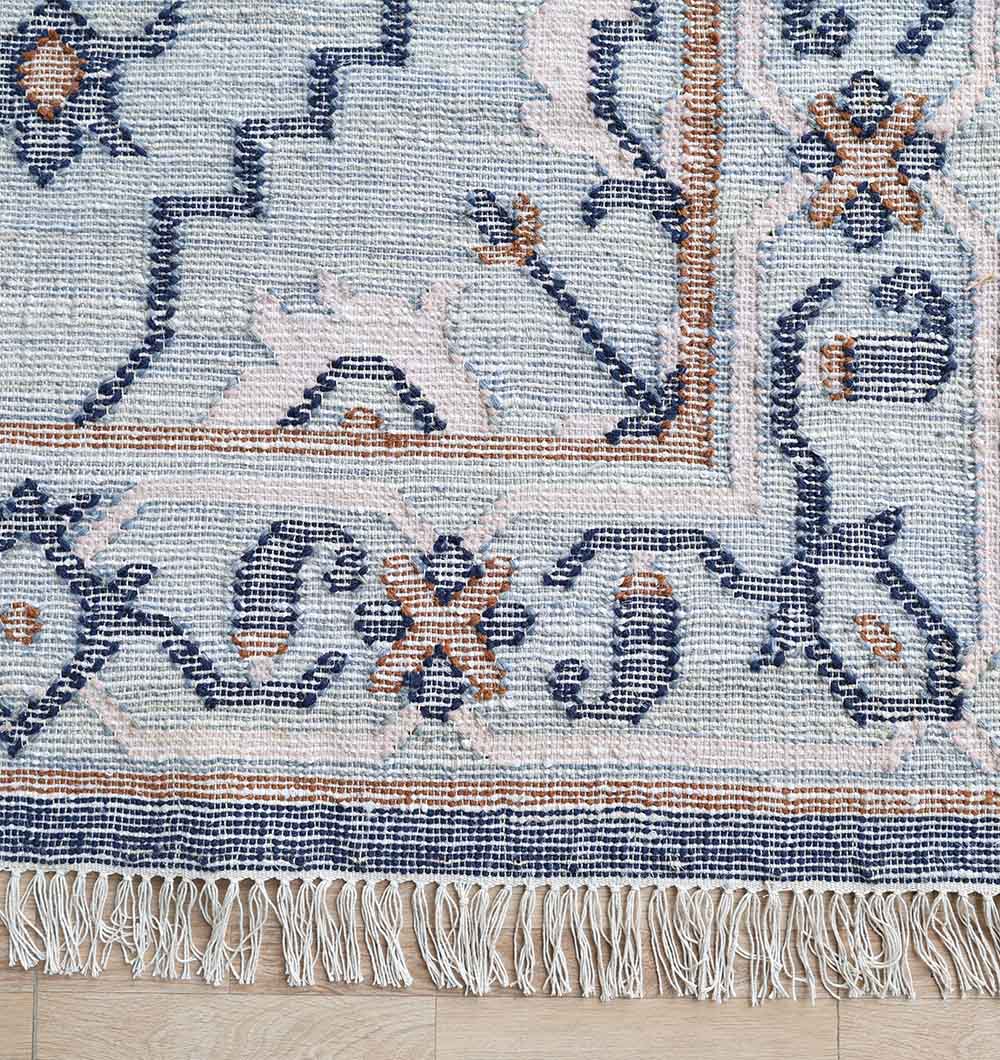A close-up of the RAMSHA HOME Kilim Rug Blue Multicolor Tribal Flatweave (KLM-015, 170x240 cm) shows its geometric patterns, floral motifs, fringe detailing, and decorative border on a light wooden floor.