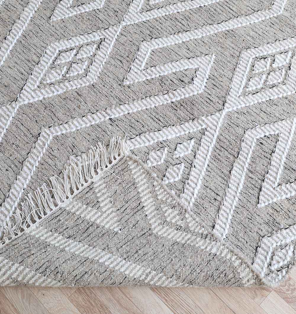 A close-up of the RAMSHA HOME Handwoven Diamond Patterned Grey Kilim Rug (KLM-017, 170x240cm) shows its white and light gray diamond design. One corner is folded, revealing the underside as it lies on a light wooden floor.