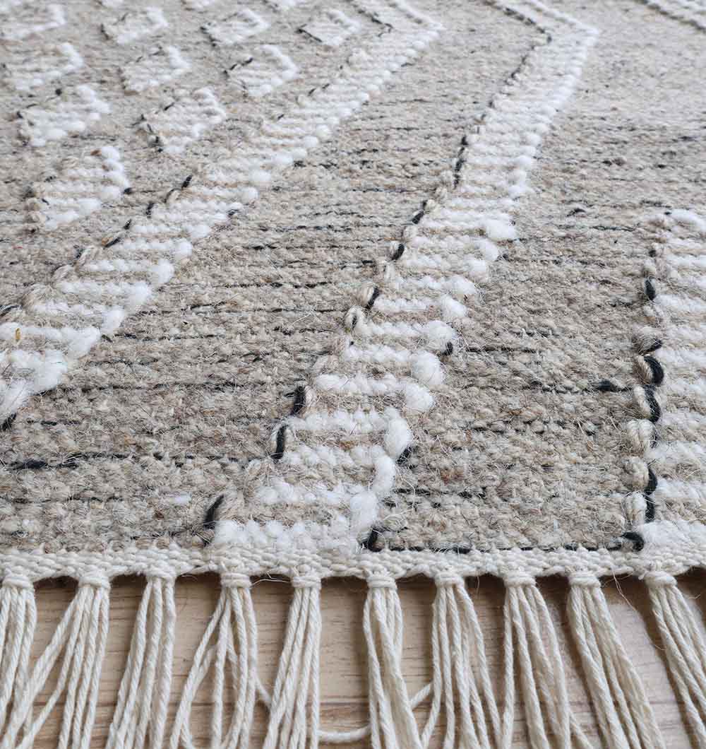 Close-up of the RAMSHA HOME Handwoven Diamond Patterned Grey Kilim Rug (KLM-017, 170x240cm) shows its textured geometric design and twisted fringe edge, highlighted in soft grey tones on a light wooden floor.