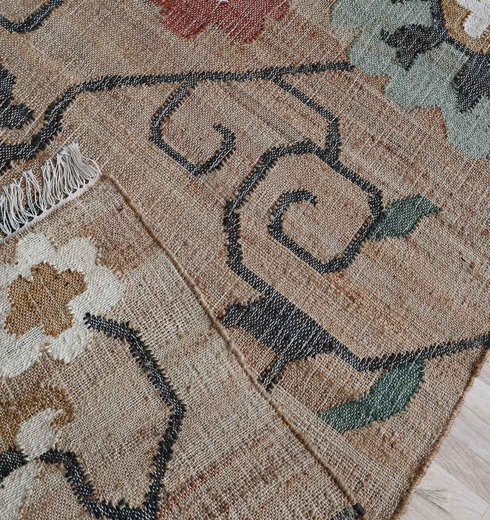 A close-up of RAMSHA HOME's Handmade Kilim Rug – Natural Floral Style Flatweave Carpet KLM-020 shows its geometric and floral patterns in black, green, red, and cream on beige, with a fringed edge—ideal for stylish neutral interiors.