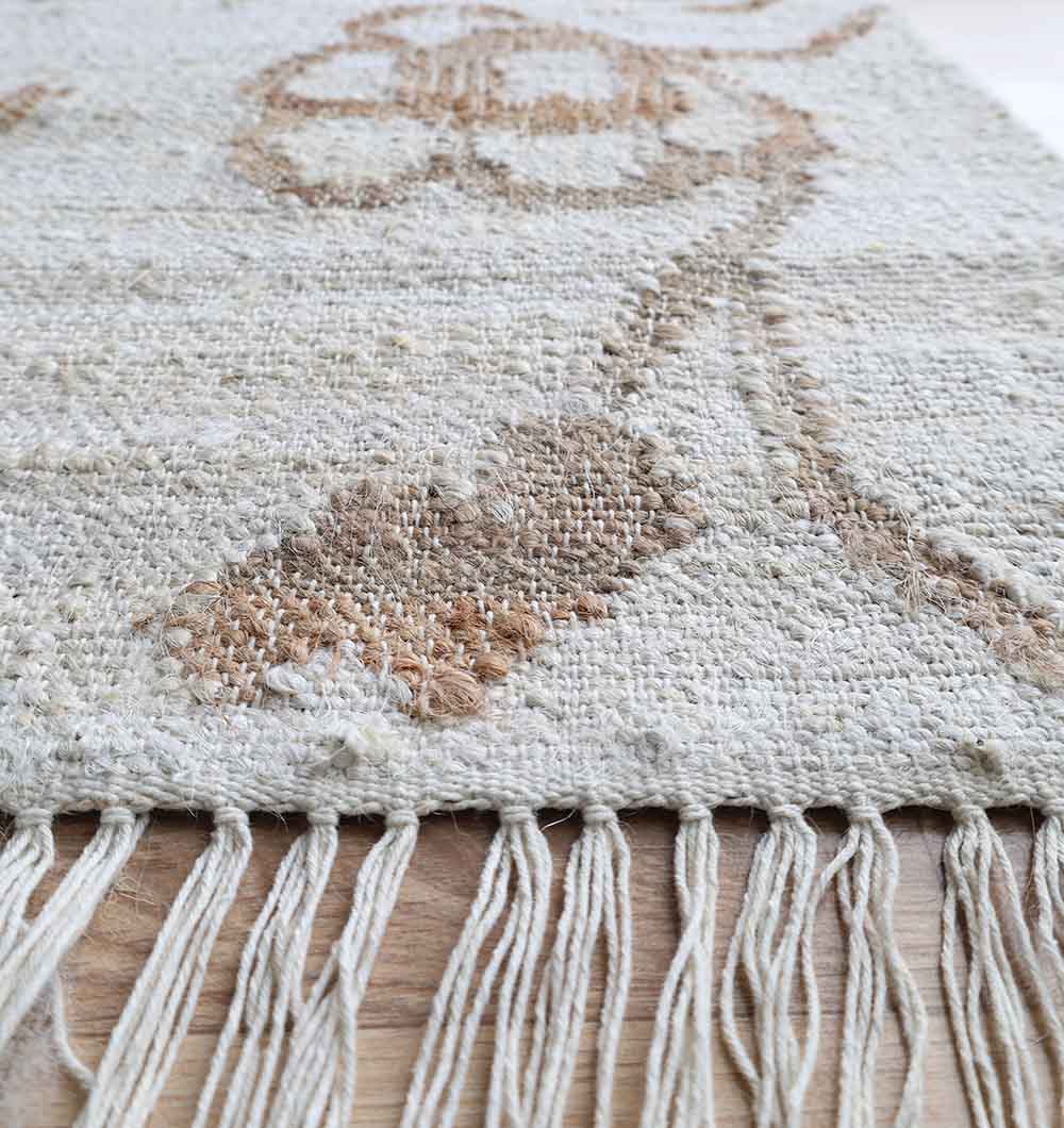 Close-up of the RAMSHA HOME Kilim Rug - Natural Handmade Flatweave Carpet (KLM 022), featuring a beige and brown floral pattern with long fringe tassels, shown on a light wooden floor.