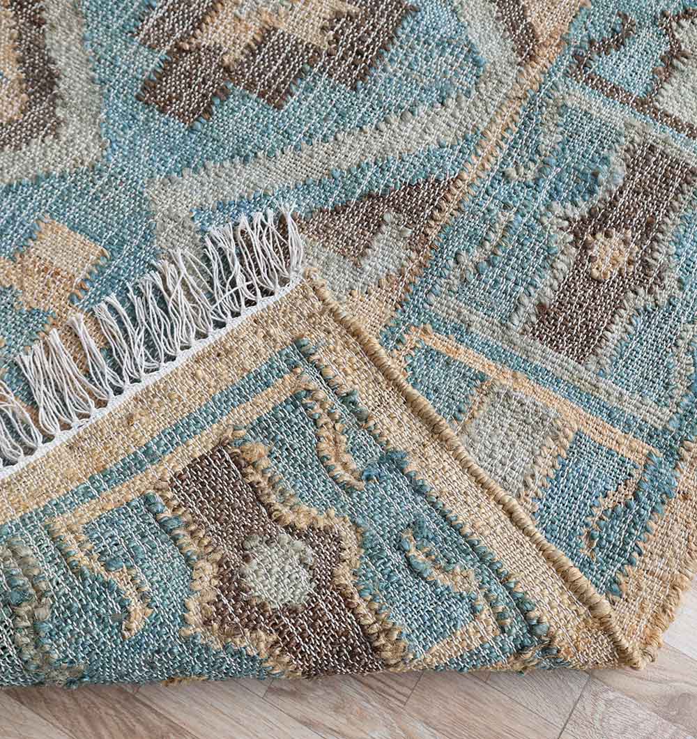 A close-up of the Handmade Kilim Rug 170x240 cm Multicolor Geometric Rug (KLM-023) by RAMSHA HOME, with a corner flipped over showing some unraveled threads along the edge, placed on a light wood floor.