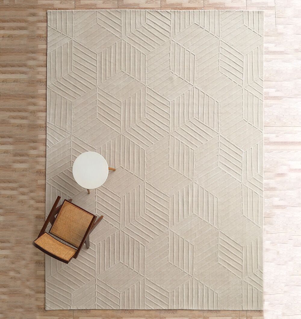 An overhead view shows the RAMSHA HOME Handmade Off White Decor Rug - LKH 010 (300x400cm) with a raised hexagonal pattern, paired with a wooden chair with woven seat and a small round white side table on light wood flooring.