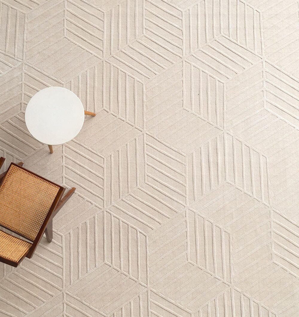 A RAMSHA HOME Handmade Off White Decor Rug (LKH 010, 300x400cm) pairs with a round white side table and a wooden chair featuring a woven cane seat and backrest, all viewed from above.