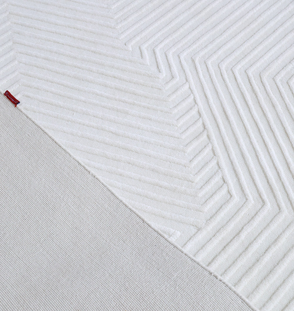 Close-up of the RAMSHA HOME Handmade Decor Area Rug - LKH 012 in ivory, showing a diagonal split between smooth knit and raised chevron textures, with a small red fabric tag near the dividing line.
