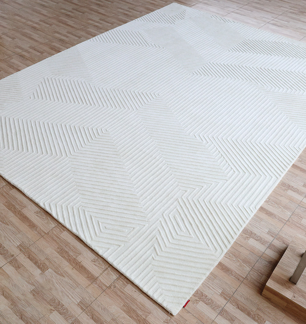 The Handmade Decor Area Rug - LKH 012 by RAMSHA HOME, featuring a large ivory geometric textured pattern, rests on a light wood-tile floor, bringing a modern vibe to the minimal, clean space.
