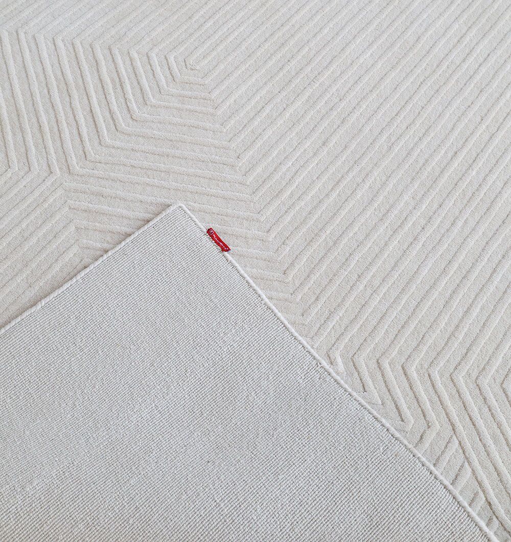 The RAMSHA HOME Handmade Area Rug - LKH-014 (200x300 cm) features a light beige Scandinavian chevron design, with one corner folded to show the plain underside and a small red fabric tag.