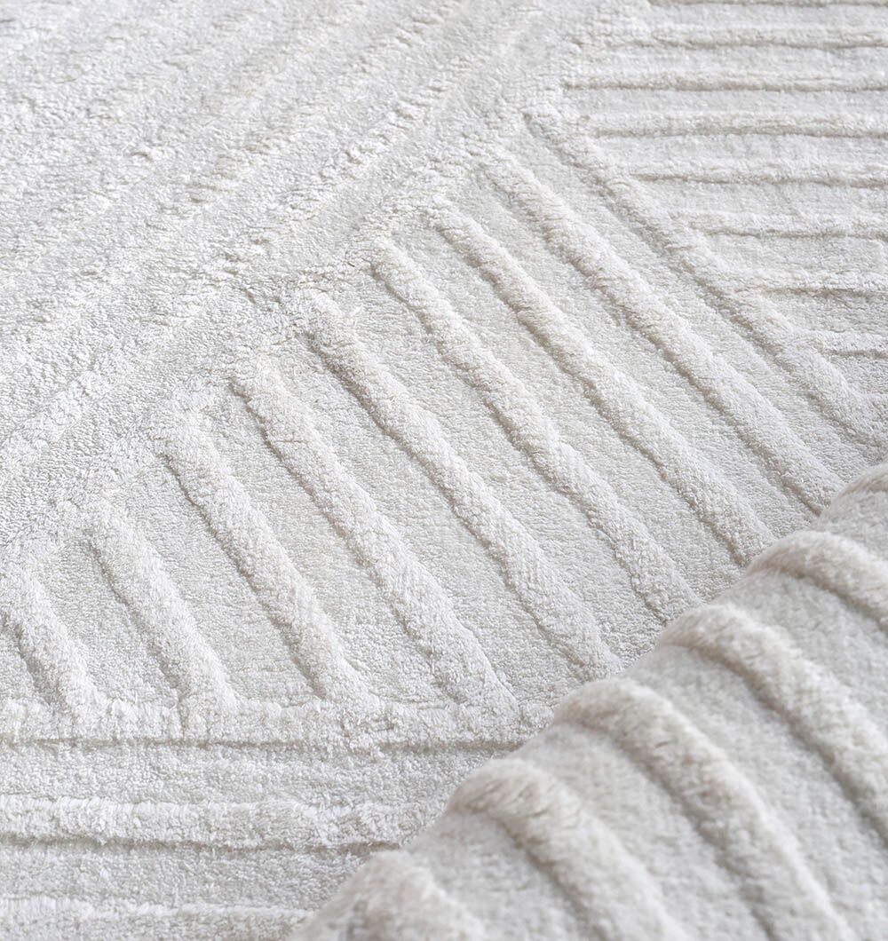 A close-up of the RAMSHA HOME Handmade Natural Color Area Rug - LKH 015, showcasing its textured off-white surface and geometric pattern with raised lines.