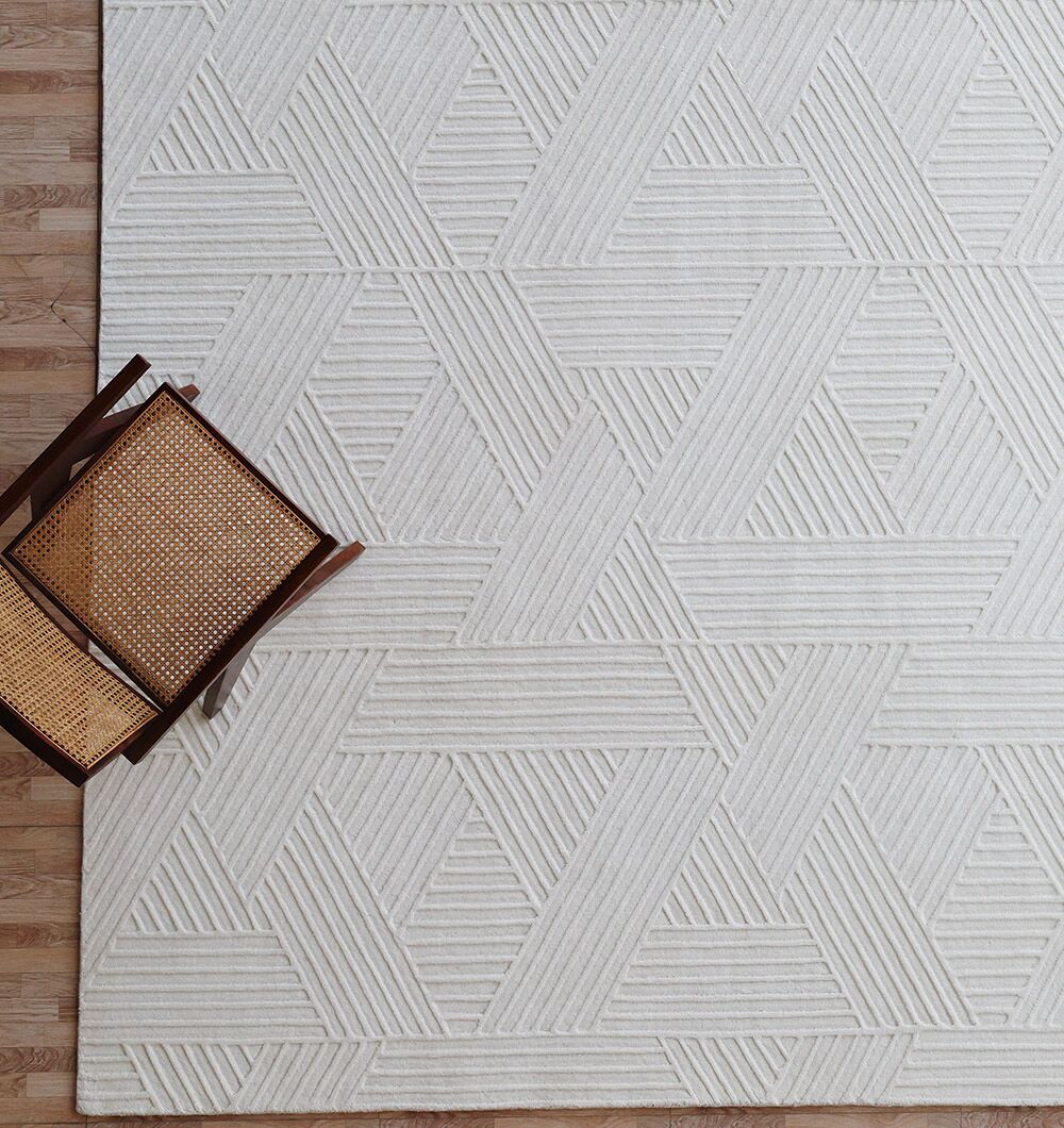 A wooden chair with a woven seat sits on the RAMSHA HOME Geometric Woven Natural Color Handmade Area Rug (LKH-016), which features an ivory, loom-knotted texture and geometric pattern, placed atop a light wood floor.