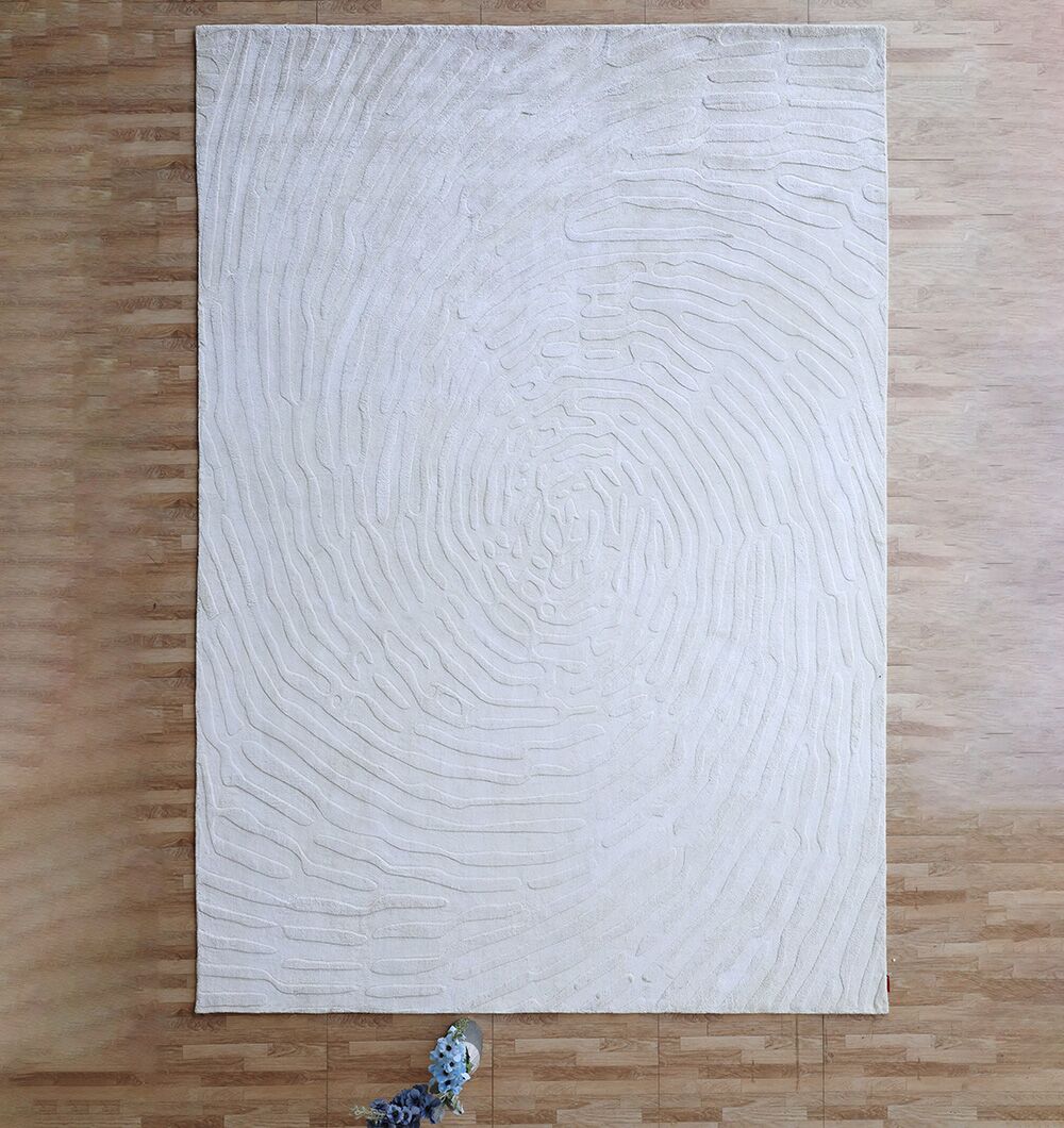 The RAMSHA HOME Decorative Handmade Area Rug (LKH-017), featuring a large ivory rectangular design with fingerprint-like raised patterns, lies on a light wood floor, accented by a small blue and white decorative object at one corner.