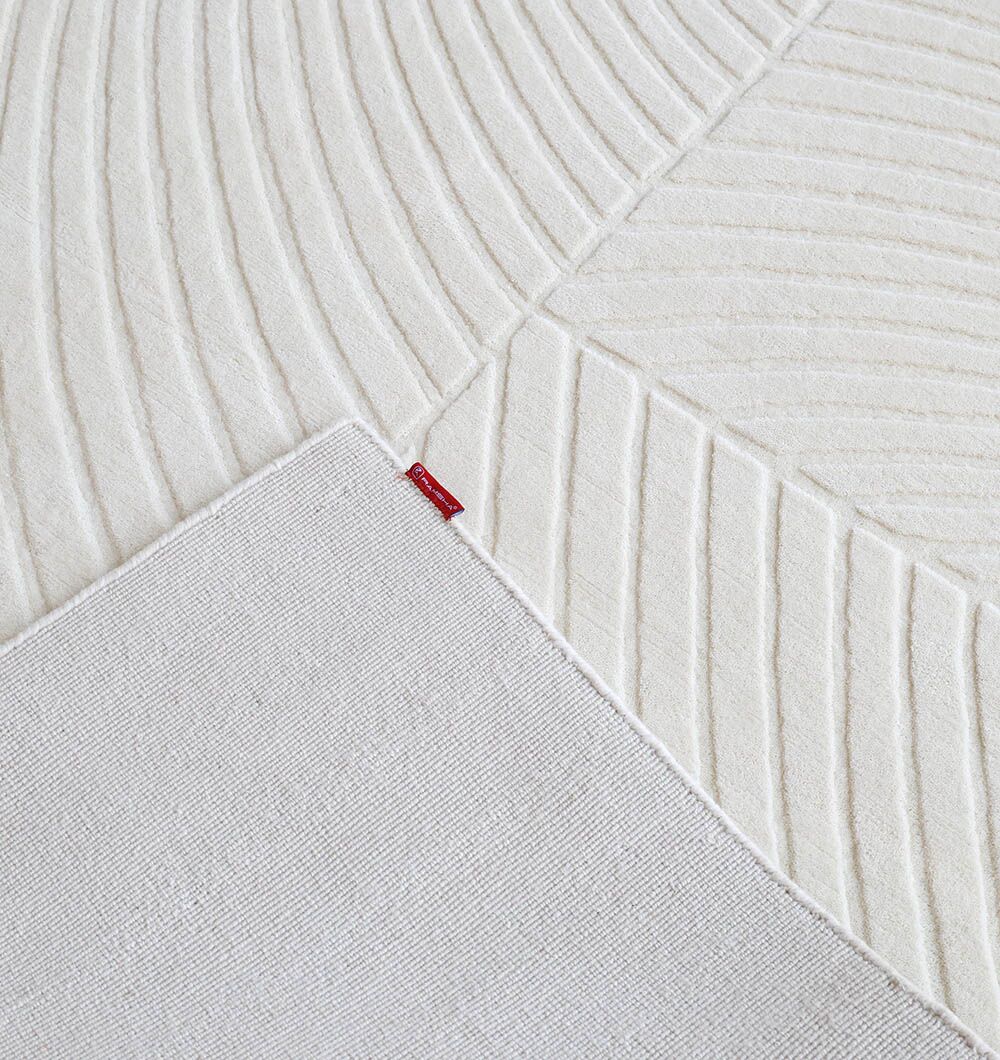 A close-up of the RAMSHA HOME Natural Color Handmade Area Rug - LKH-018 (200x300 cm) shows its textured geometric pattern with raised lines, one corner folded to reveal the plain underside and a small red tag.