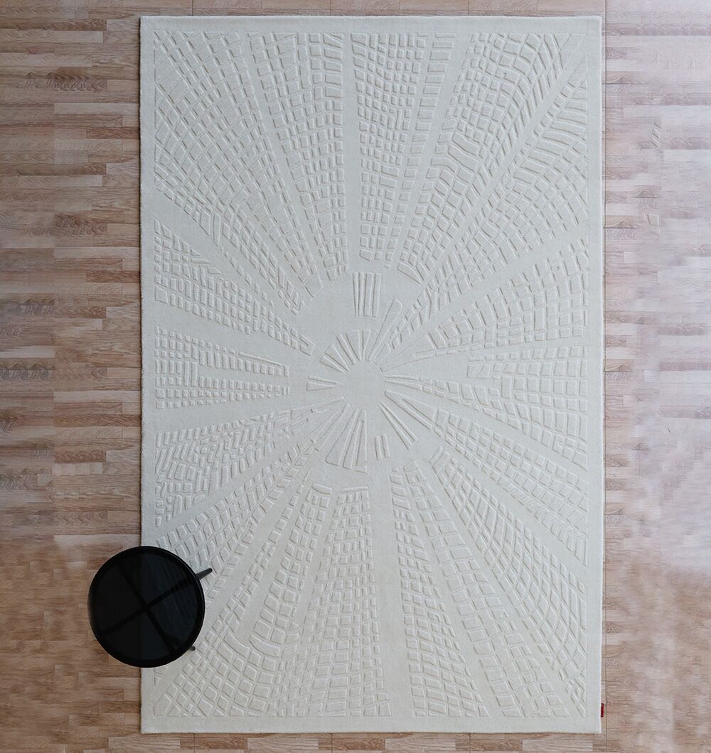 The RAMSHA HOME Handmade Decorative Area Rug - LKH-019 (200x300 cm), featuring a beige textured geometric design, lies on a light wood floor with a small round black side table at its lower left corner.