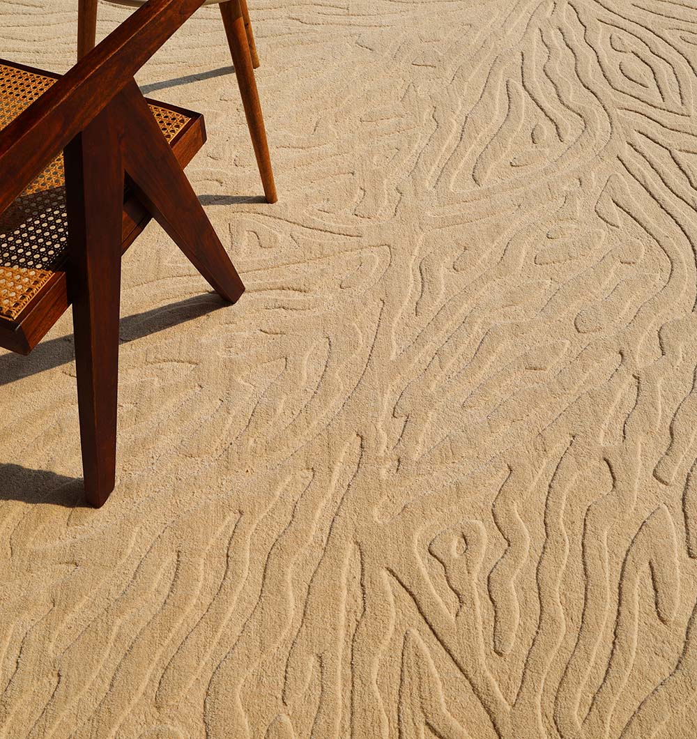 A wooden chair with a woven seat is placed on the Handmade Beige Rug with Organic Tree-Inspired Pattern LKH-025 by RAMSHA HOME, a modern area rug featuring textured patterns that evoke the graceful lines of tree growth, lending a sophisticated yet natural charm to the space.