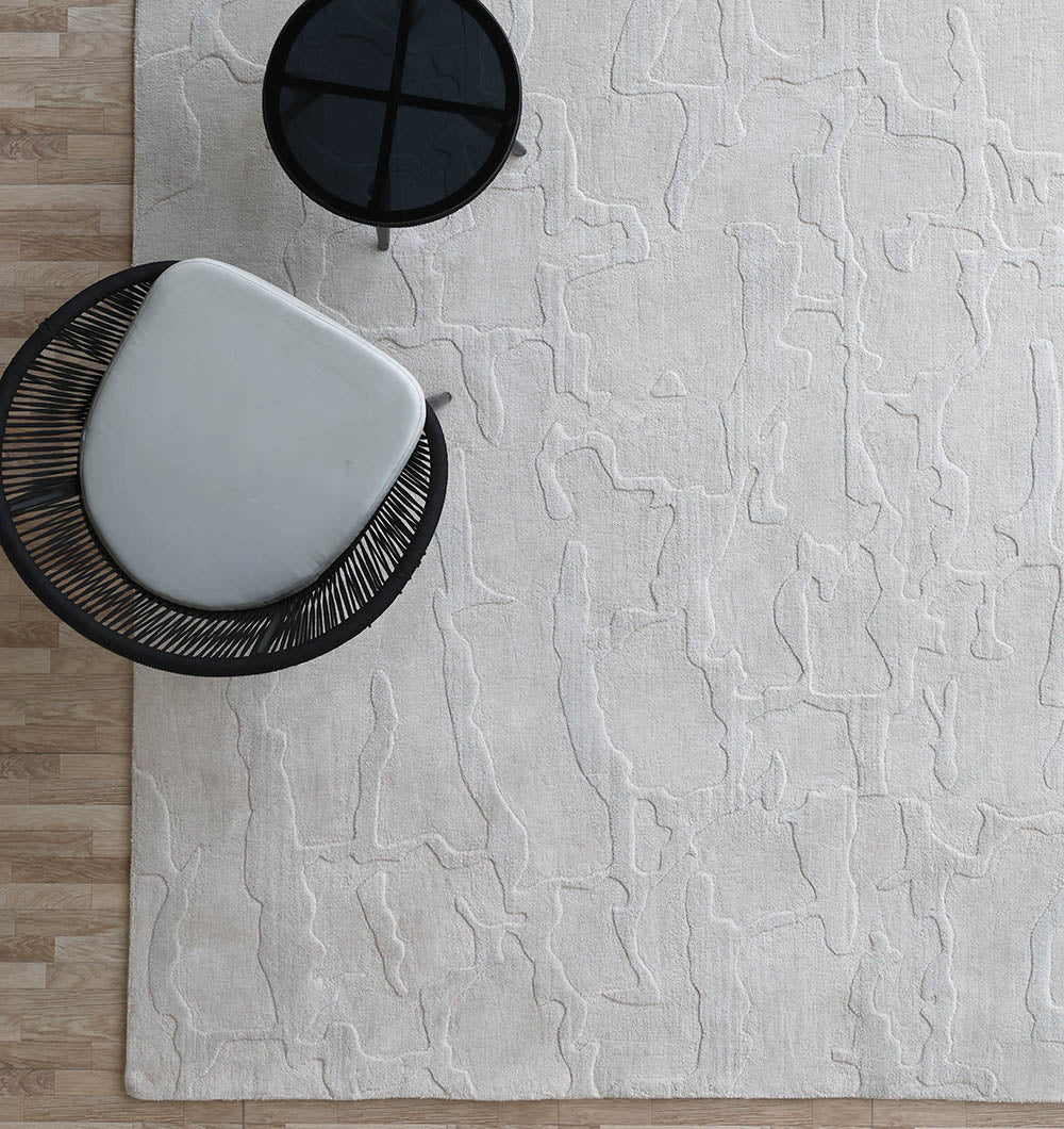 A modern living space featuring the RAMSHA HOME Decorative Light Brown Color Area Rug (LKH-027, 300x400 cm), a round black wire-frame chair with a gray cushion, and a small round black side table on a wooden floor.