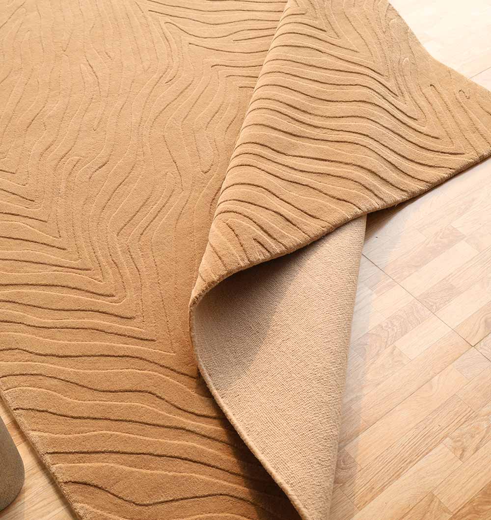 The Decorative Handmade Beige Color Area Rug - LKH-028 by RAMSHA HOME, featuring a subtle wavy pattern, is shown partially folded on a light wood floor to display its underside.