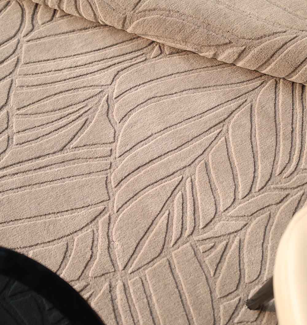 Close-up of the Rectangle Handmade Decorative Grey Color Area Rug - LKH-030 by RAMSHA HOME, featuring a raised leaf pattern; partially rolled at the top with a black circular item and light furniture leg visible in the corners.