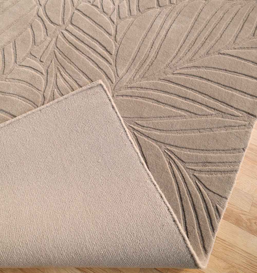 A close-up of the Rectangle Handmade Decorative Grey Color Area Rug (LKH-030) by RAMSHA HOME shows its embossed leaf pattern, a folded corner revealing the plain textured underside, and the rug placed on a light wooden floor.