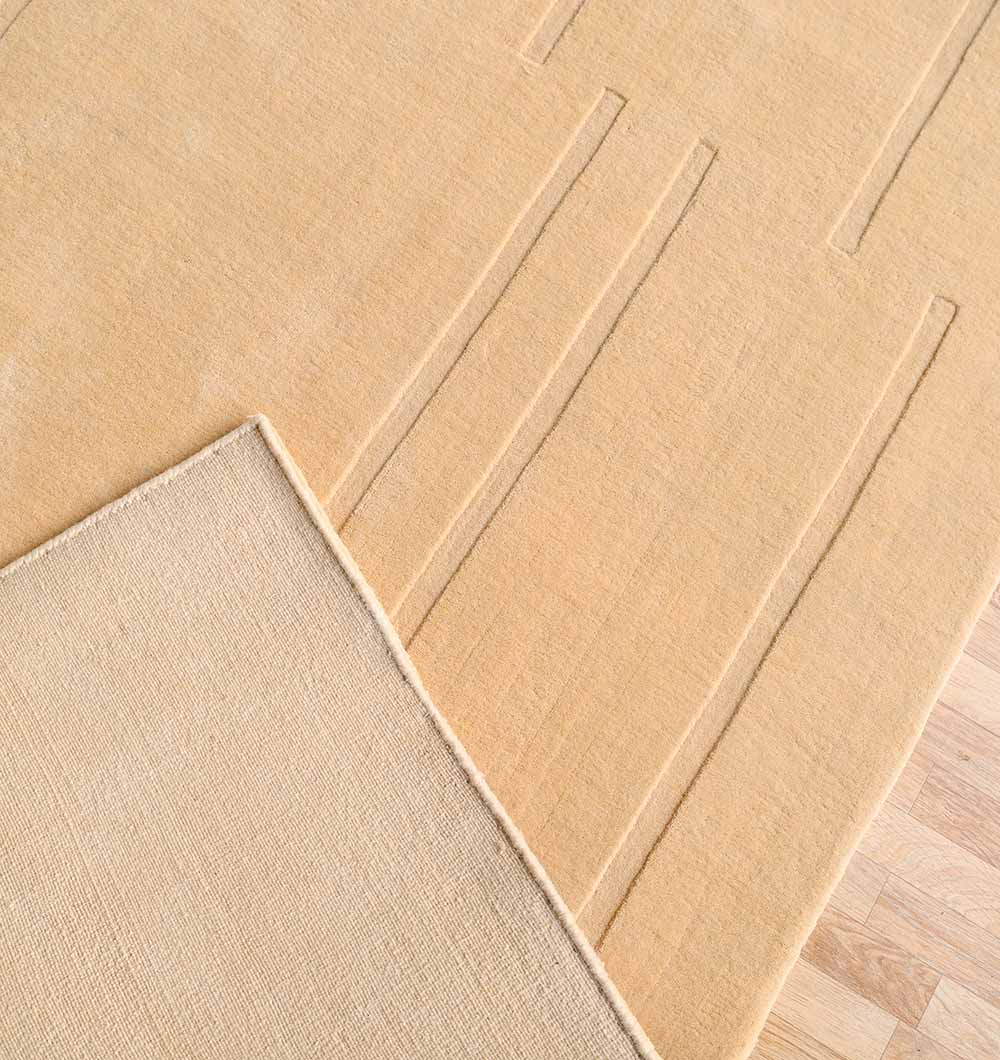 The RAMSHA HOME Rectangle Handmade Decorative Beige Color 250x350 cm Area Rug (LKH-031) features a subtle, textured linear pattern—ideal for minimalist interiors. The photo shows one corner flipped, revealing its plain underside and the wooden floor below.