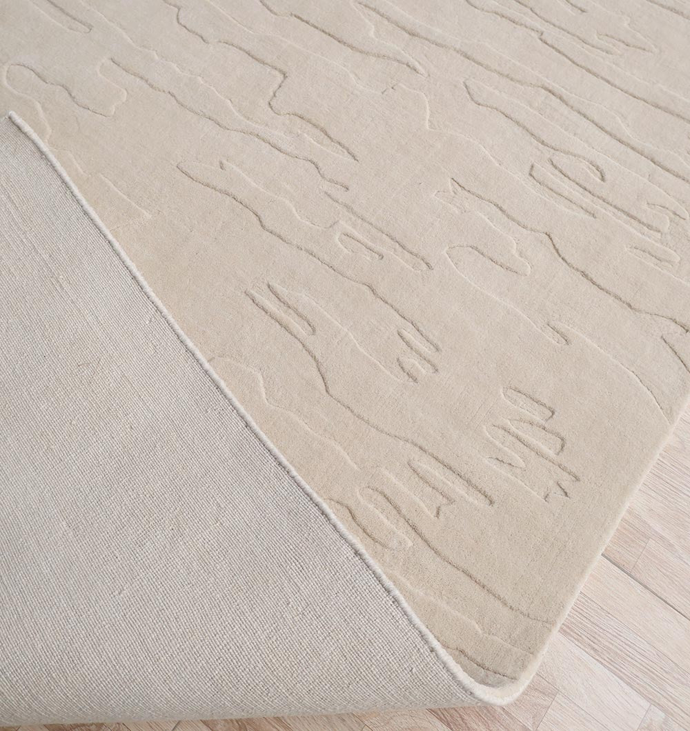 A close-up of the RAMSHA HOME Rectangle Handmade Decorative Beige Color 300x400 cm Area Rug (LKH-032) shows its subtle wavy raised pattern, with a corner folded to reveal the plain underside and wool texture on a light wood floor.