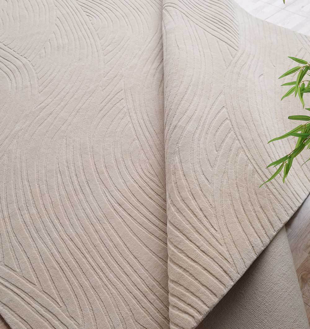 A close-up of the RAMSHA HOME Decorative Rectangle Handmade Beige Area Rug (300x400 cm, LKH-033) shows raised wavy patterns and a folded corner revealing the underside, with green plant leaves visible in the upper right.