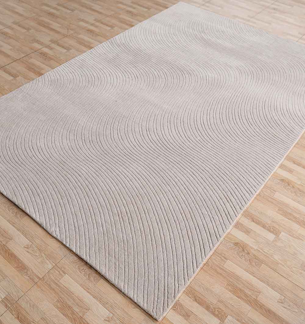 The RAMSHA HOME Decorative Rectangle Handmade Lt. Grey 200x300 cm Area Rug (LKH-037) lies on a wood-patterned floor, adding modern style and subtle texture with its raised, wavy line pattern.