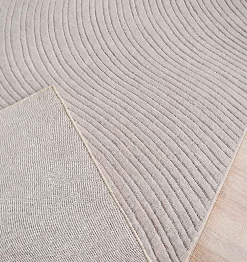 A close-up of the RAMSHA HOME Decorative Rectangle Handmade Lt. Grey 200x300 cm Area Rug (LKH-037) with raised curved wave patterns, one corner flipped to show the plain underside, resting on a light wood floor.