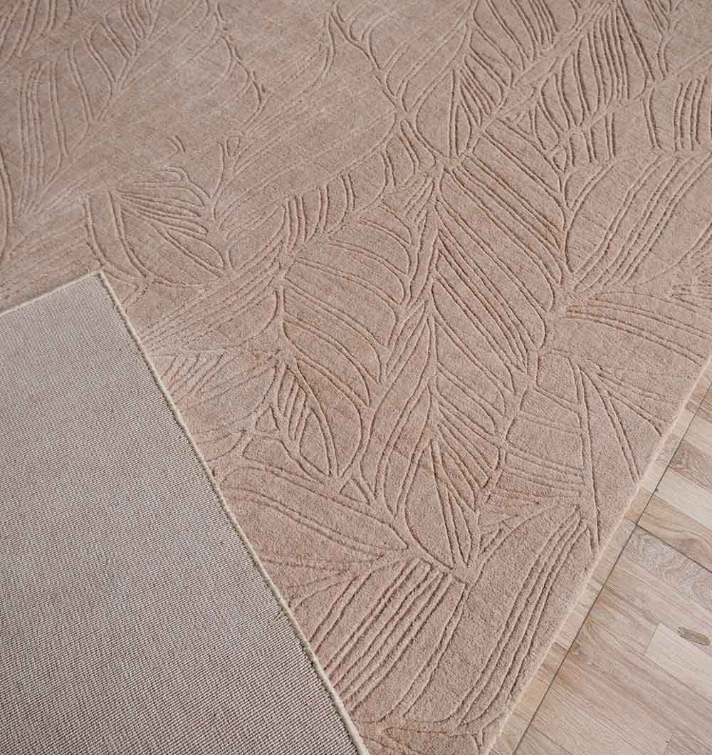 A RAMSHA HOME Decorative Rectangle Handmade Beige Area Rug (200x300 cm, LKH-038) lies on a light wood floor; one corner is flipped, showing its plain underside and the subtle leaf pattern on top.