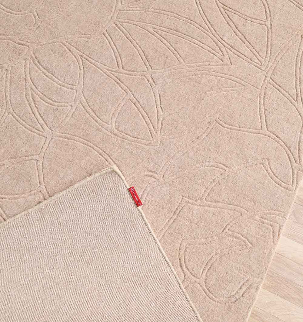 A close-up of the RAMSHA HOME Rectangle Handmade Beige Color 200x300 cm Area Rug (LKH-041) shows its subtle floral pattern, visible texture, and a flipped corner with a red tag, highlighting its quality craftsmanship.