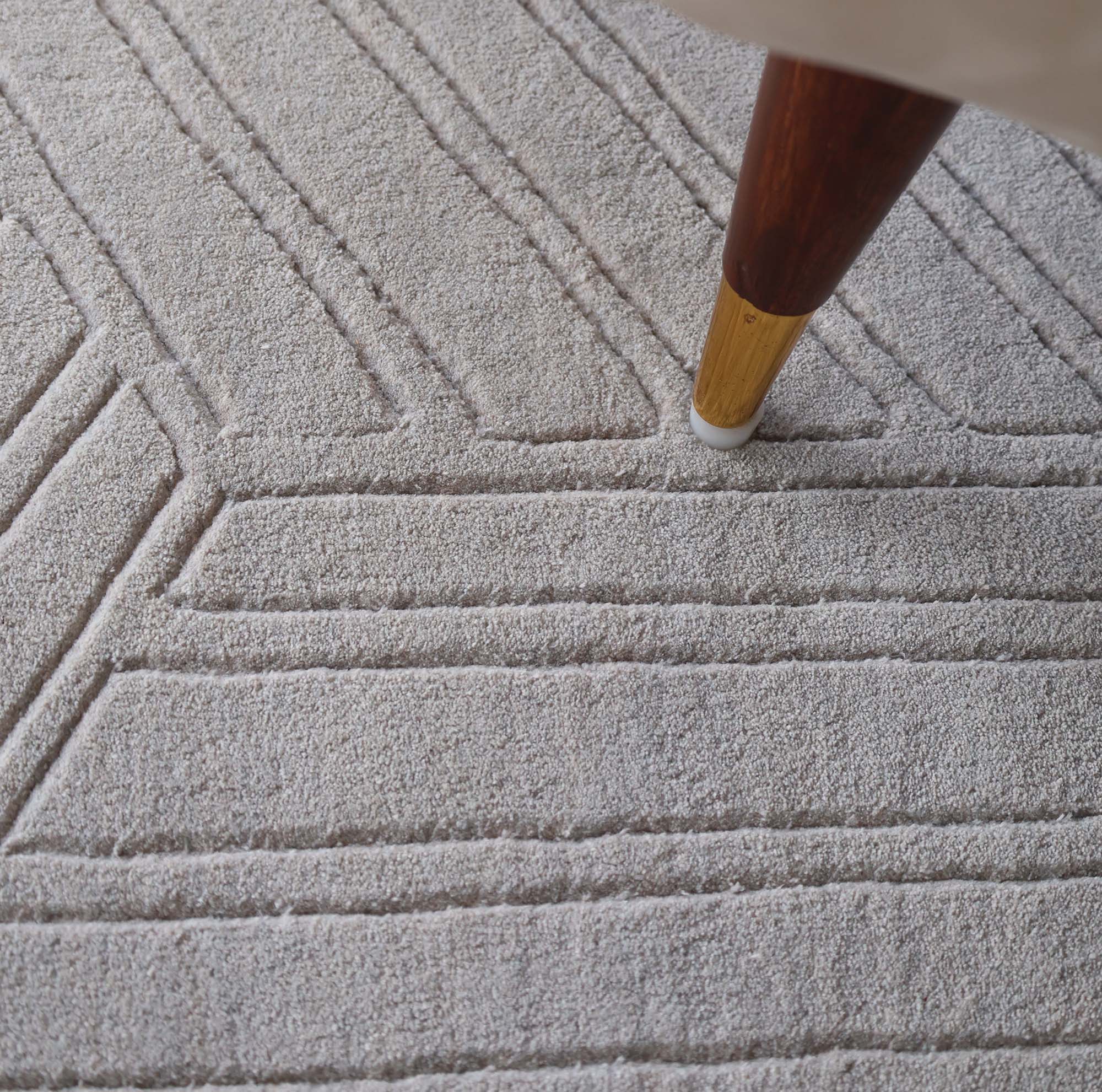 Close-up of RAMSHA HOME's Home Decor Light Grey Handmade Area Rug 300x400 cm (LKH-044), highlighting its subtle geometric texture and a wooden-brass furniture leg in the upper right corner.