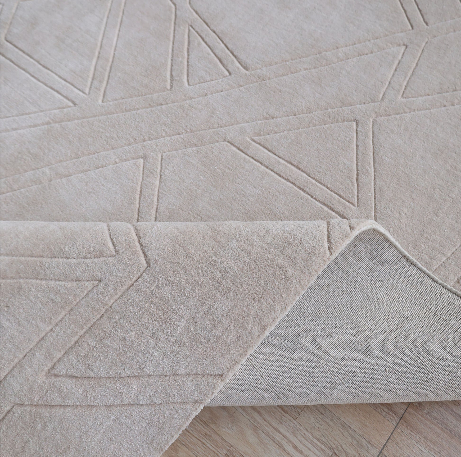 A close-up of the RAMSHA HOME Rectangle Home Decor Cream Color Handmade Area Rug 300x400 cm (LKH-045), featuring geometric patterns and textured surface, is shown partially folded on a light wooden floor.