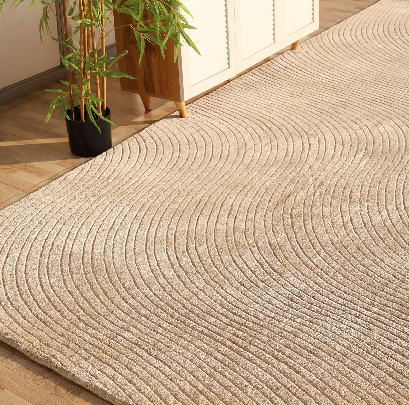 The RAMSHA HOME Handmade beige Wave Modern Abstract High-Low Area Rug 250x350 cm (LKH-049) adds texture to the light wood floor, complemented by a potted bamboo plant and white cabinet in the sunlit, modern space.