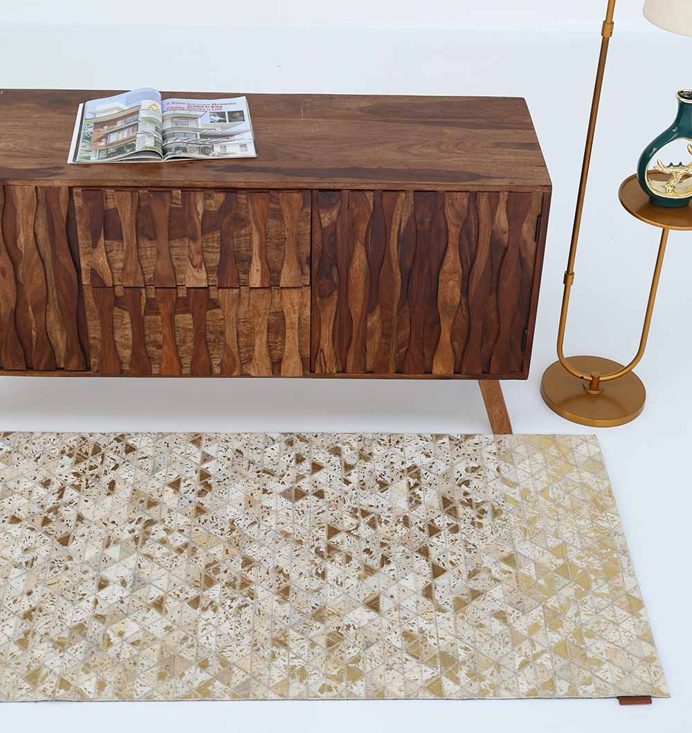 The Amazing Grey & Tan Color Playroom Leather Rug - LR 006 is placed before a wooden cabinet with textured doors. Nearby are a brass floor lamp, a glass decor piece, and a magazine on the cabinet, all atop a white floor.