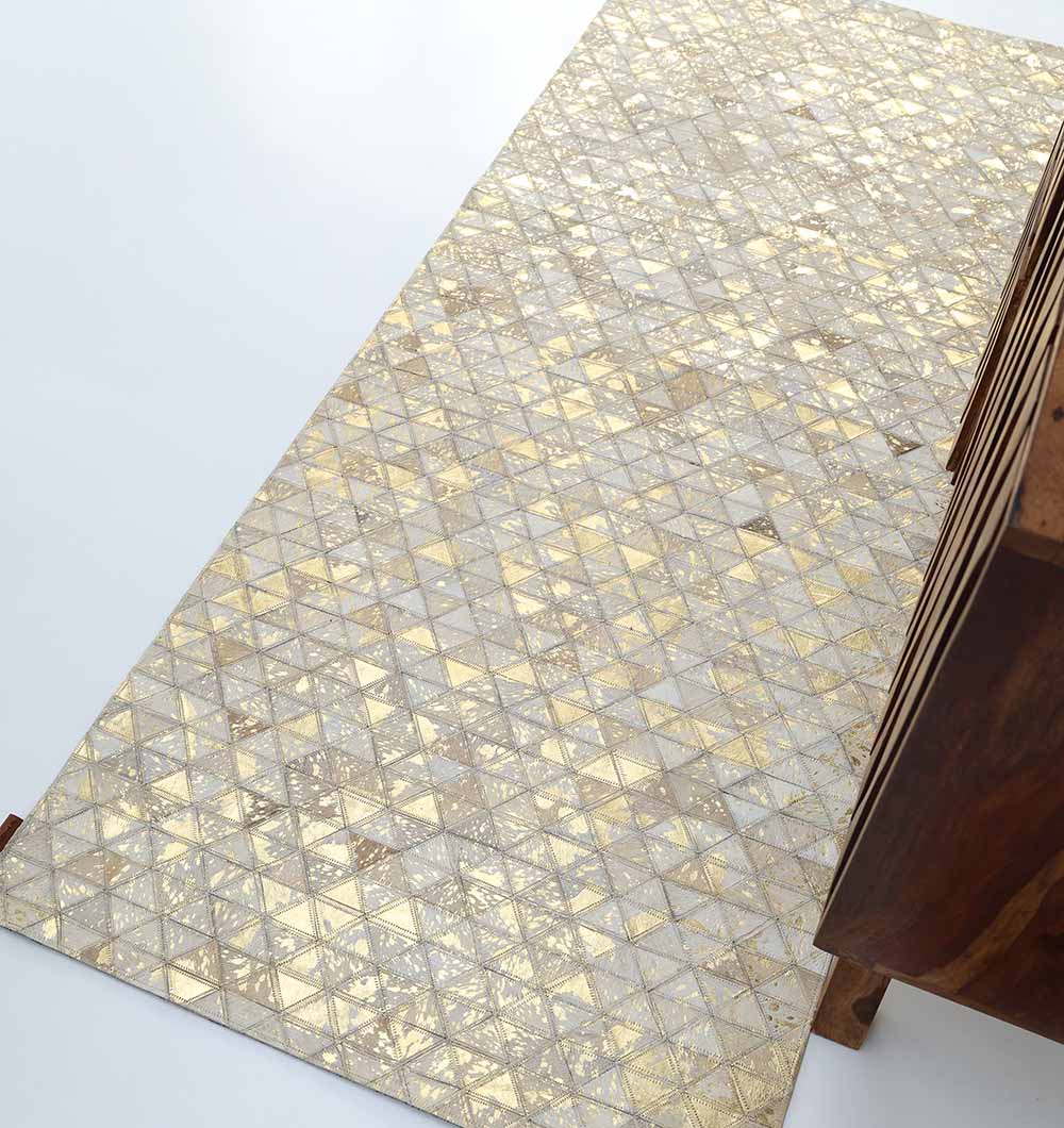The Amazing Grey & Tan Color Playroom Leather Rug - LR 006 features gold and beige triangles and diamonds, displayed on a light floor beside wooden furniture.