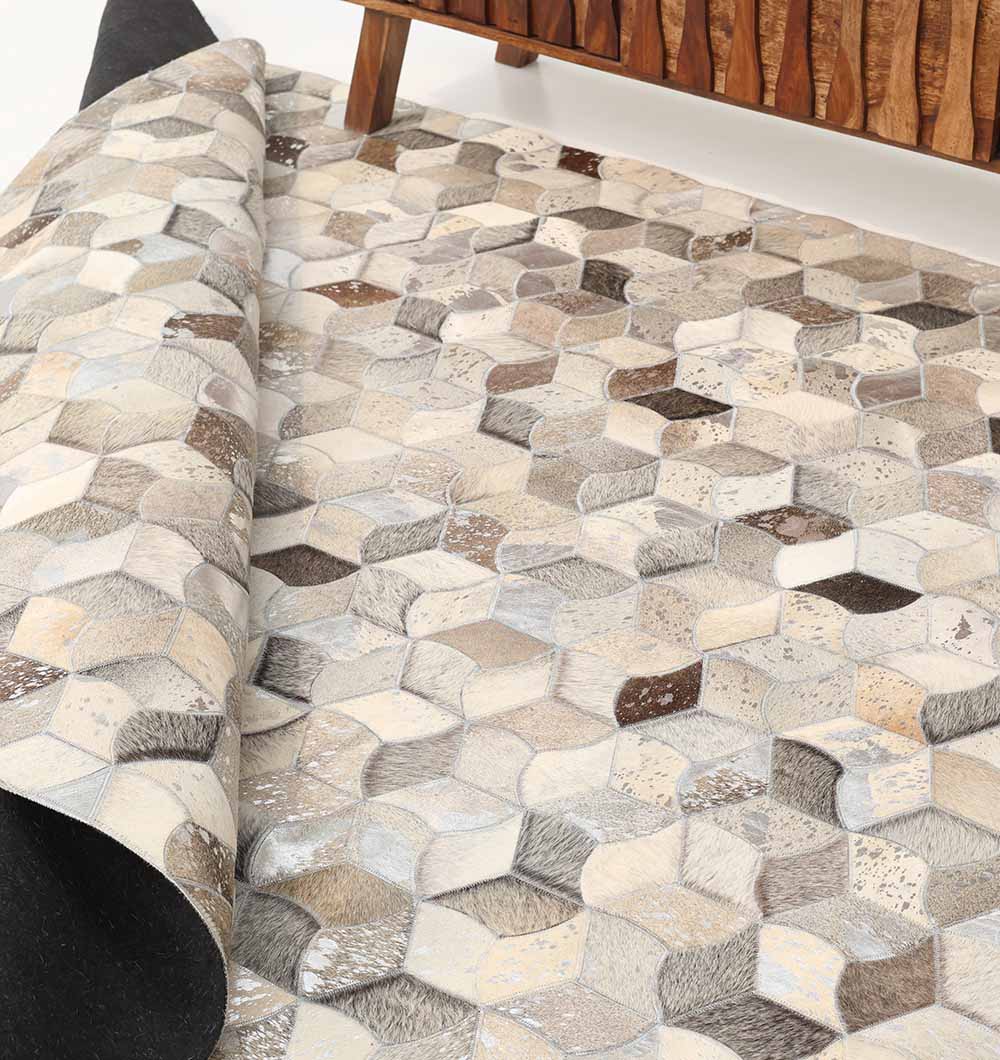 A close-up of the RAMSHA HOME Amazing Bedroom & Hallway Grey Color Leather Rug - LR 007, with interlocking cubes and neutral tones, partially rolled by a chevron wooden cabinet, emphasizes its sophisticated geometric style.
