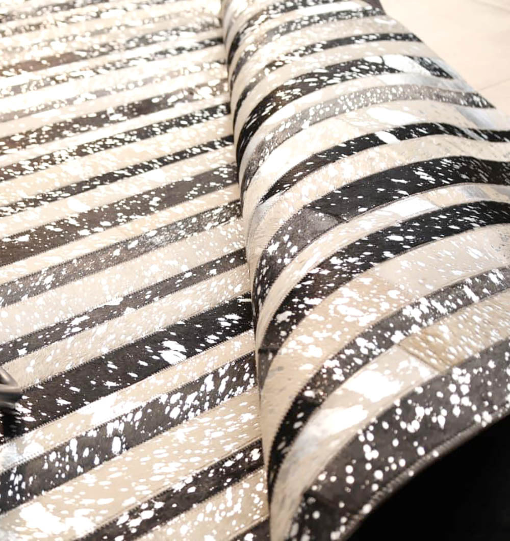 A close-up of the RAMSHA HOME Striped Abstract Black & Ivory Leather Area Rug LR-009 shows glossy, textured leather with black, beige, and white horizontal stripes and a bold splattered paint effect.