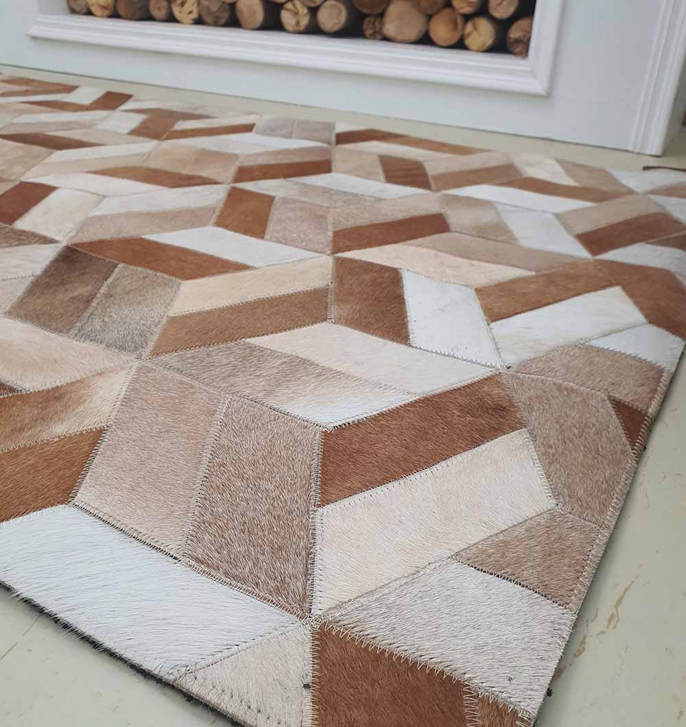 The RAMSHA HOME Geometric Cube Pattern Handmade Leather Area Rug LR-012 features tan, brown, and cream leather patches in a 3D cube design, shown on a light floor near a fireplace with stacked firewood.
